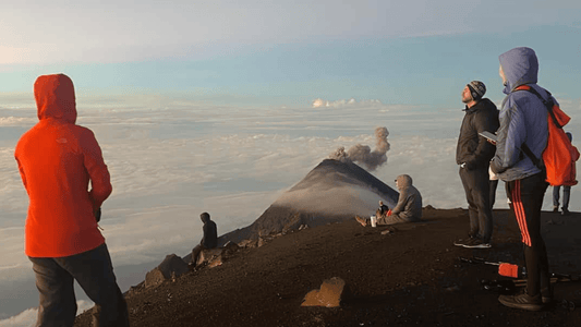 Group of adventurers gazing at a volcano surrounded by clouds, embodying the thrill of exploration and nature's beauty. Why Choose Global Trekker for Your Next Adventure? - Adventure Compass Blog By Global Trekker.