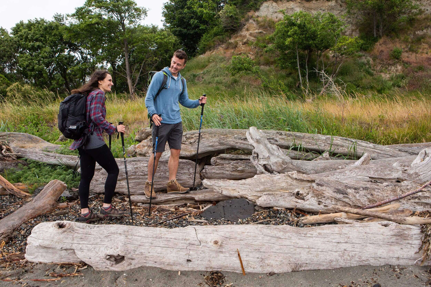 Two hikers navigating a beach with walking poles, wearing backpacks and breathable apparel. Featured Products - Adventure Gear From Global Trekker.