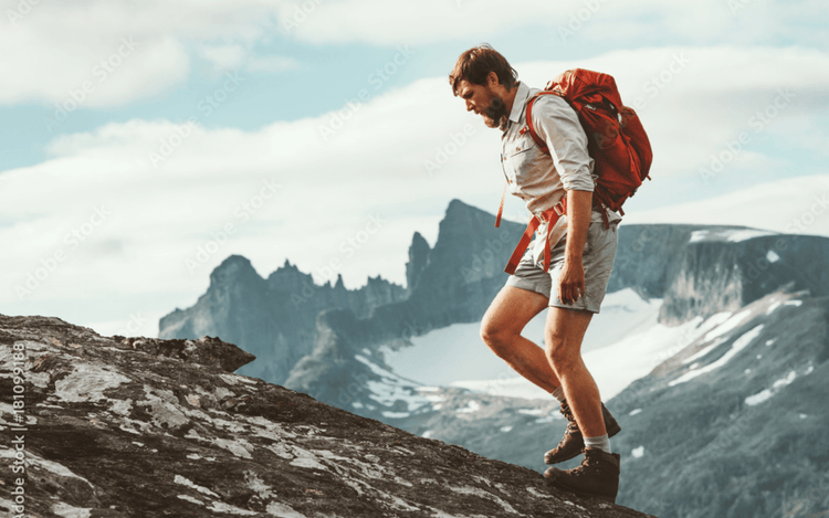 Man hiking on rocky terrain with a red backpack, showcasing men's outdoor apparel in an adventurous landscape - Men's Outdoor Apparel - Adventure Gear From Global Trekker.